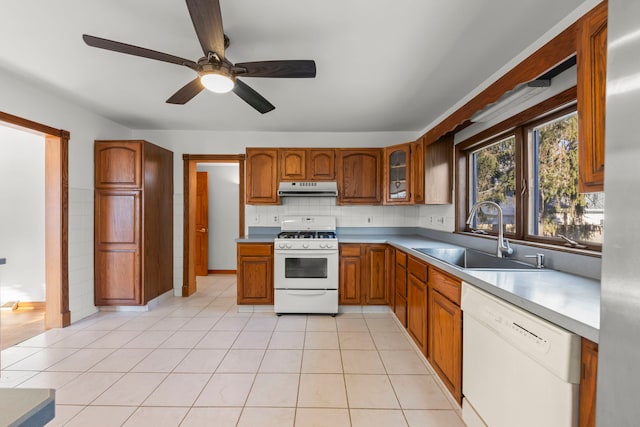 kitchen with light tile patterned floors, brown cabinets, exhaust hood, white appliances, and a sink