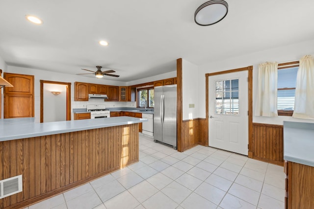 kitchen with visible vents, range hood, white appliances, a peninsula, and wainscoting