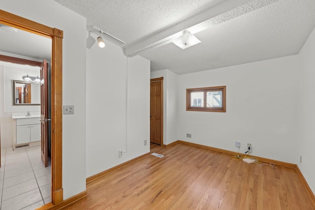 unfurnished bedroom featuring visible vents, a sink, a textured ceiling, light wood-style floors, and baseboards