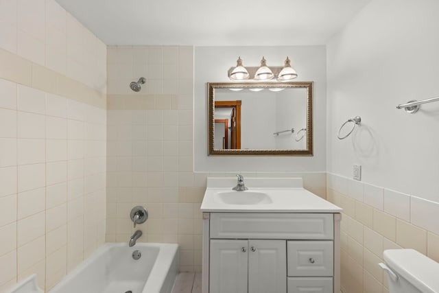 bathroom with vanity, wainscoting, tile walls, toilet, and shower / bathtub combination