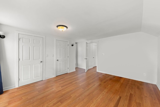 unfurnished bedroom with light wood finished floors, baseboards, and vaulted ceiling