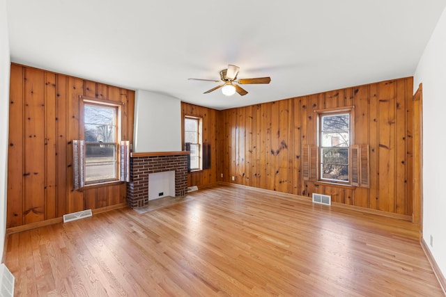 unfurnished living room with visible vents, a brick fireplace, ceiling fan, and wood finished floors