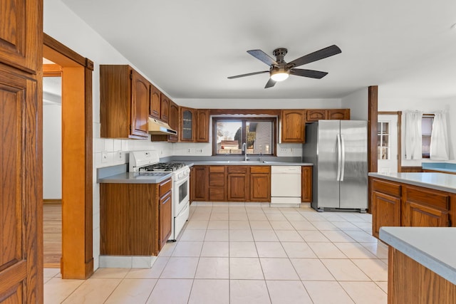 kitchen with brown cabinets, under cabinet range hood, a sink, white appliances, and ceiling fan