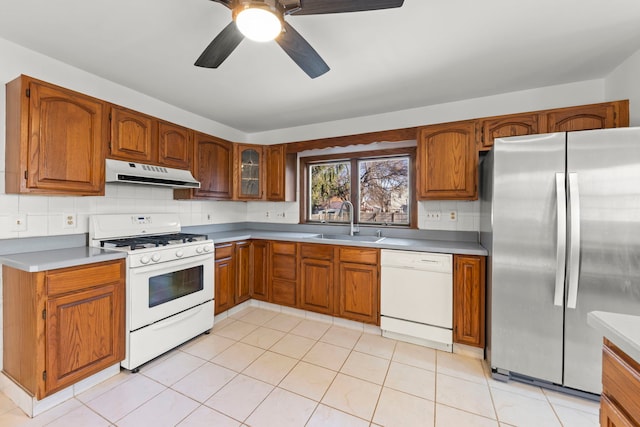 kitchen with a sink, white appliances, exhaust hood, and brown cabinetry