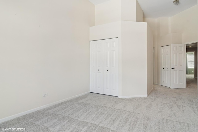 unfurnished bedroom featuring baseboards, light colored carpet, and a high ceiling