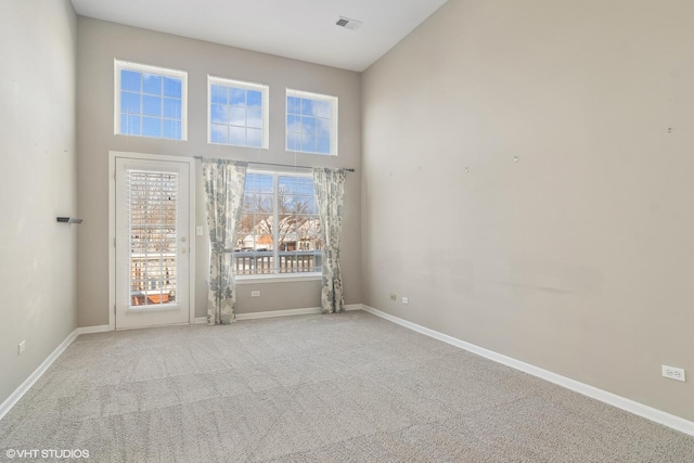 carpeted spare room featuring a high ceiling, visible vents, and baseboards