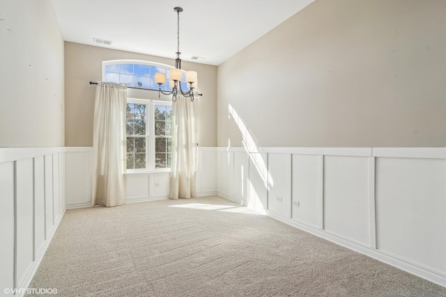 empty room featuring a notable chandelier, a wainscoted wall, visible vents, and light colored carpet