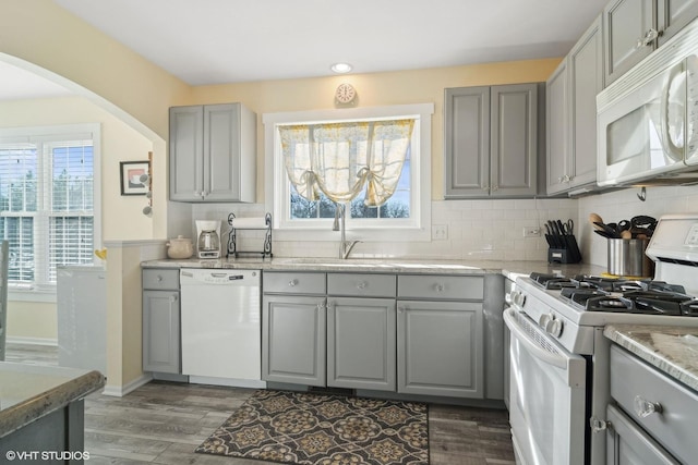 kitchen featuring white appliances, backsplash, gray cabinets, and a sink