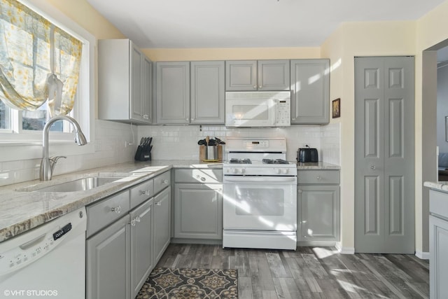 kitchen with gray cabinets, decorative backsplash, dark wood-type flooring, a sink, and white appliances