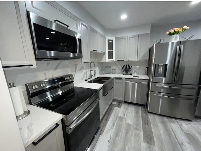 kitchen with tasteful backsplash, light wood-style flooring, glass insert cabinets, stainless steel appliances, and a sink