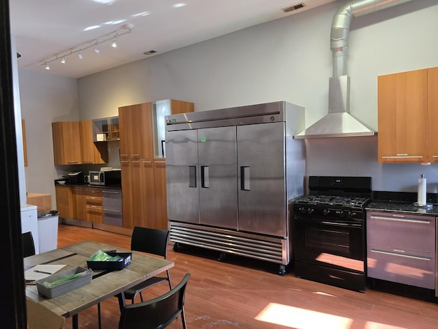2147 W Belmont Ave, Chicago, IL 60618 - kitchen featuring visible vents, appliances with stainless steel finishes, brown cabinetry, wall chimney range hood, and light wood-type flooring