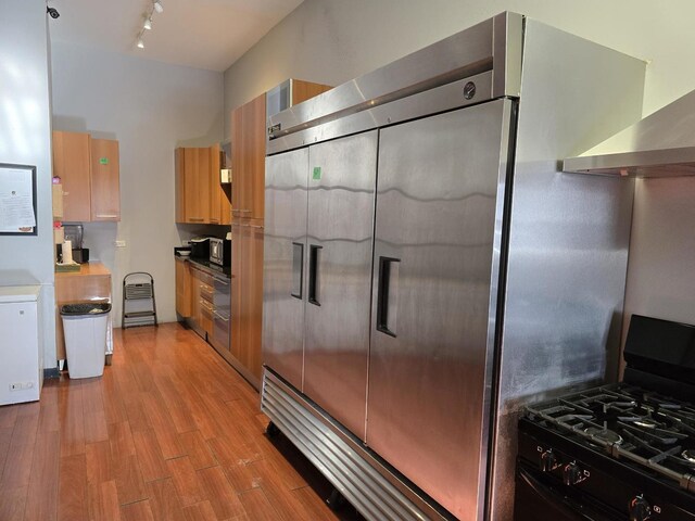 2147 W Belmont Ave, Chicago, IL 60618 - kitchen with light wood-style flooring, brown cabinets, black range with gas stovetop, stainless steel built in refrigerator, and wall chimney range hood