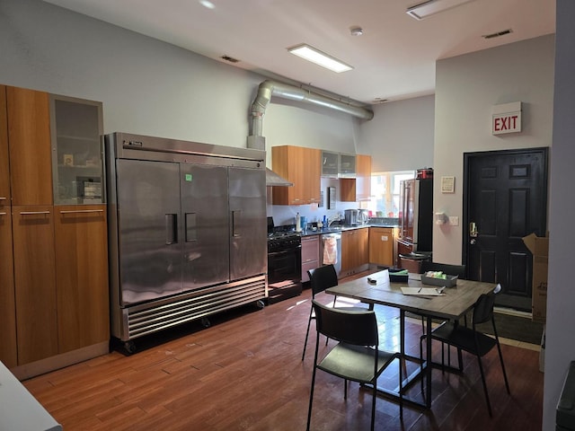 2147 W Belmont Ave, Chicago, IL 60618 - kitchen featuring brown cabinets, stainless steel appliances, glass insert cabinets, dark wood-type flooring, and wall chimney range hood