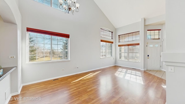 entryway featuring high vaulted ceiling, a notable chandelier, plenty of natural light, and wood finished floors