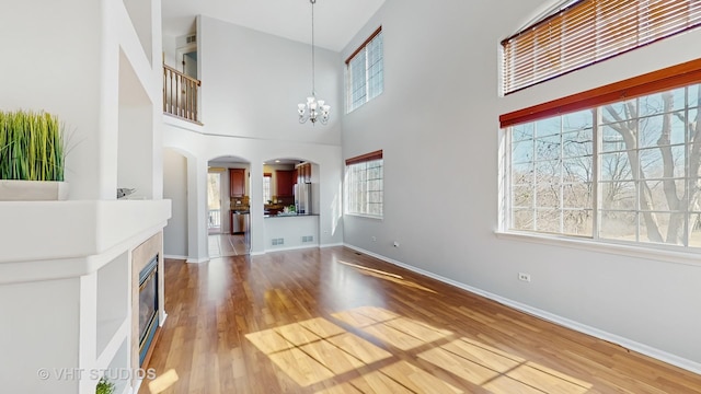 unfurnished living room featuring baseboards, arched walkways, wood finished floors, a high ceiling, and a chandelier