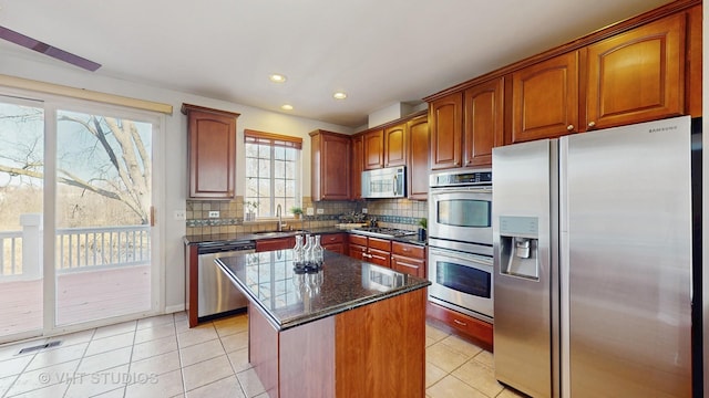 kitchen with light tile patterned flooring, stainless steel appliances, a kitchen island, decorative backsplash, and dark stone countertops