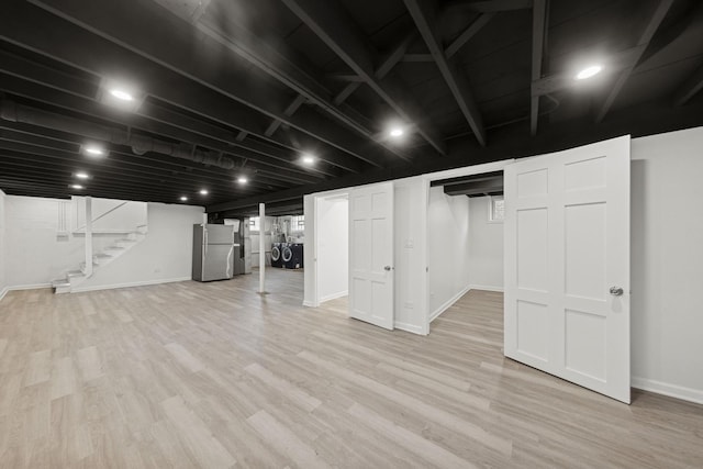 finished basement featuring light wood-style flooring, freestanding refrigerator, stairway, and baseboards