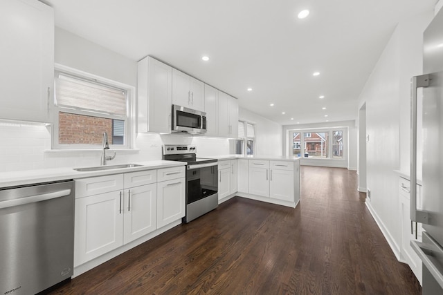 kitchen featuring stainless steel appliances, a peninsula, a sink, decorative backsplash, and dark wood-style floors