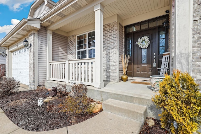 doorway to property featuring an attached garage, covered porch, and brick siding