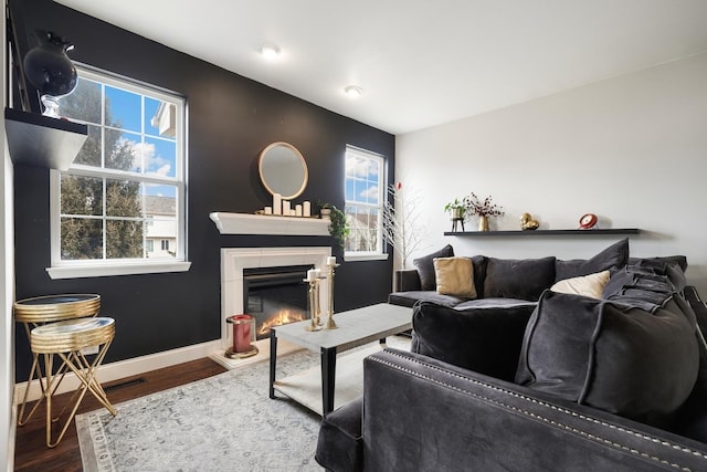 living room featuring visible vents, baseboards, wood finished floors, and a glass covered fireplace