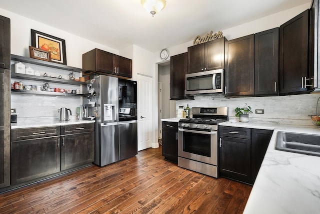 kitchen featuring dark wood finished floors, appliances with stainless steel finishes, light stone countertops, open shelves, and backsplash