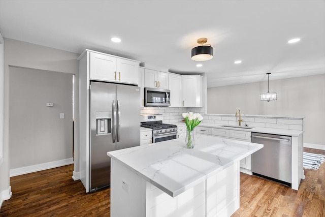 kitchen featuring appliances with stainless steel finishes, decorative light fixtures, a sink, and a kitchen island