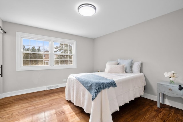 bedroom with a barn door, visible vents, baseboards, and wood finished floors