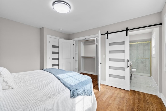 bedroom with a closet, a barn door, ensuite bath, wood finished floors, and baseboards