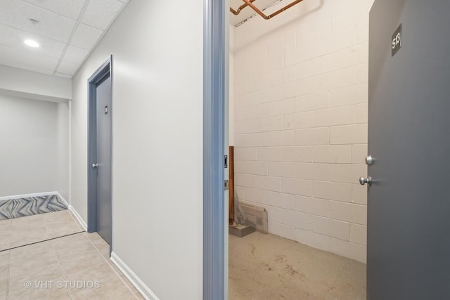 hall with concrete block wall, recessed lighting, light tile patterned flooring, a drop ceiling, and baseboards