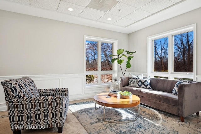 living area with light tile patterned floors, a drop ceiling, a decorative wall, recessed lighting, and wainscoting