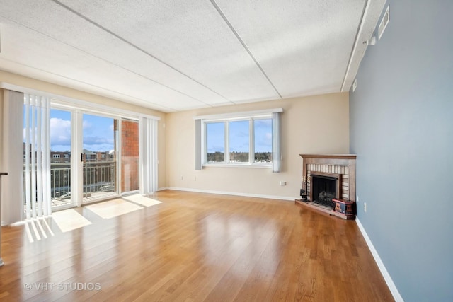 unfurnished living room featuring a brick fireplace, plenty of natural light, baseboards, and wood finished floors