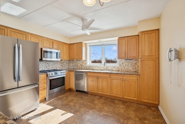 kitchen with a sink, a ceiling fan, appliances with stainless steel finishes, decorative backsplash, and light stone countertops