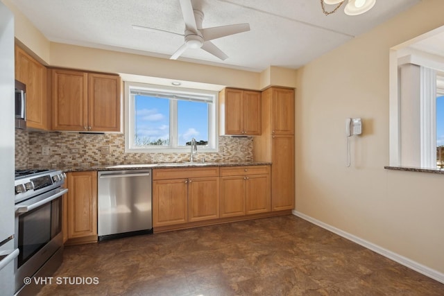 kitchen with stainless steel appliances, tasteful backsplash, a sink, dark stone countertops, and baseboards