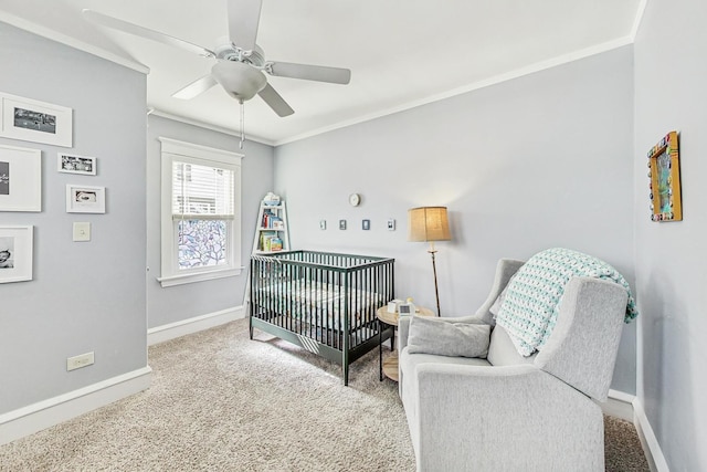 bedroom featuring a ceiling fan, baseboards, ornamental molding, a crib, and carpet