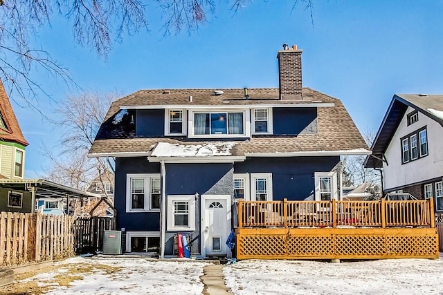 snow covered back of property with a chimney, fence, a deck, and stucco siding