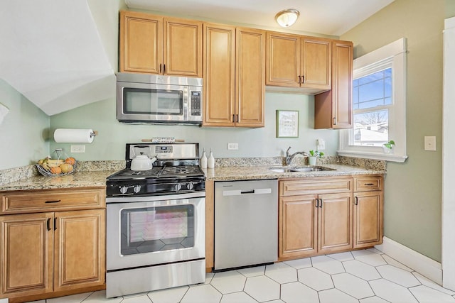 kitchen with appliances with stainless steel finishes, a sink, light stone counters, and baseboards