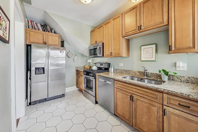 kitchen featuring light stone counters, stainless steel appliances, brown cabinetry, vaulted ceiling, and a sink