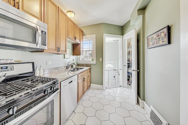 kitchen with light stone counters, stainless steel appliances, a sink, visible vents, and baseboards