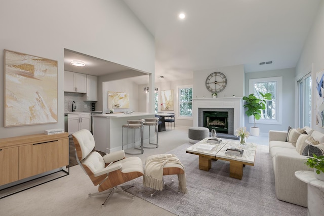 living room with high vaulted ceiling, light carpet, a fireplace, visible vents, and baseboards