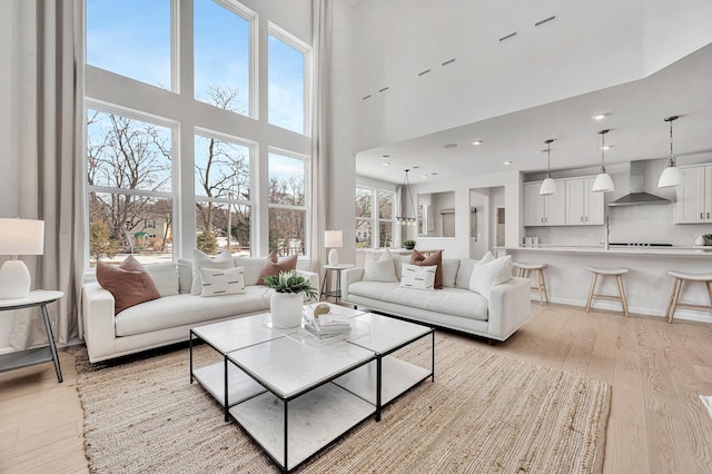 living room featuring a healthy amount of sunlight, recessed lighting, a towering ceiling, and light wood-style floors