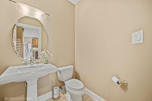 half bath featuring a sink, tile patterned flooring, toilet, and baseboards