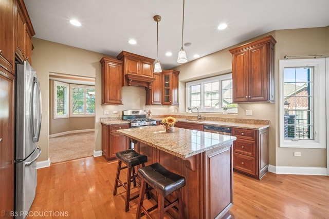 kitchen with a sink, a kitchen island, appliances with stainless steel finishes, brown cabinetry, and glass insert cabinets