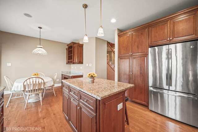 kitchen with light stone counters, pendant lighting, light wood-style floors, freestanding refrigerator, and a kitchen island