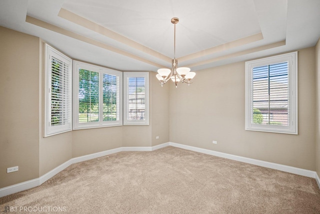 empty room featuring a chandelier, a raised ceiling, light colored carpet, and baseboards