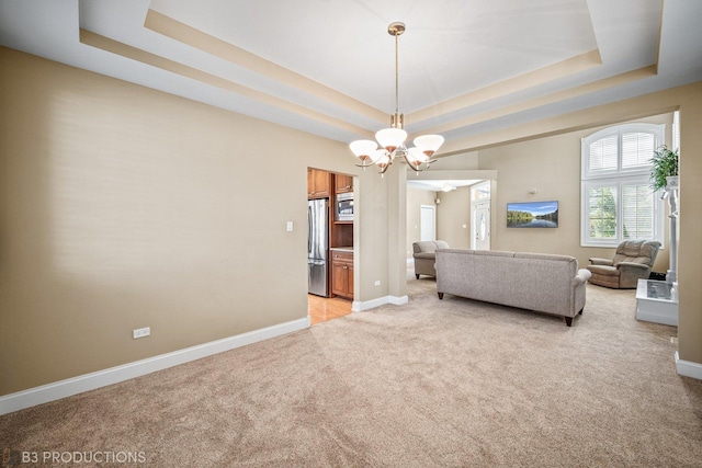 living room with baseboards, a raised ceiling, a notable chandelier, and light colored carpet