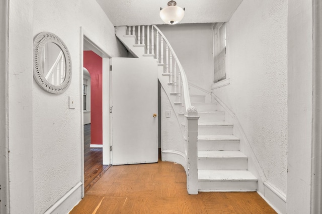 staircase with a textured wall, baseboards, and wood finished floors