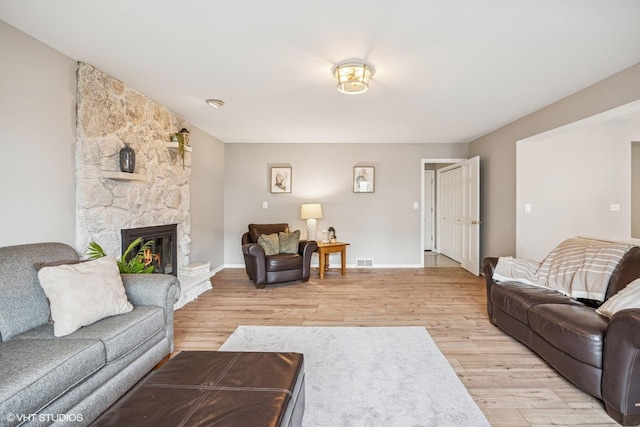 living room featuring light wood-type flooring, visible vents, a stone fireplace, and baseboards