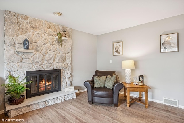 living area featuring baseboards, a fireplace, visible vents, and wood finished floors