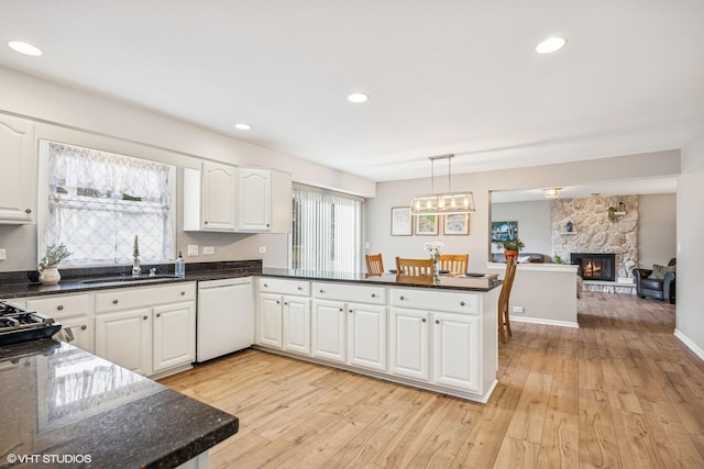 kitchen with a fireplace, light wood-style flooring, white dishwasher, a sink, and a peninsula