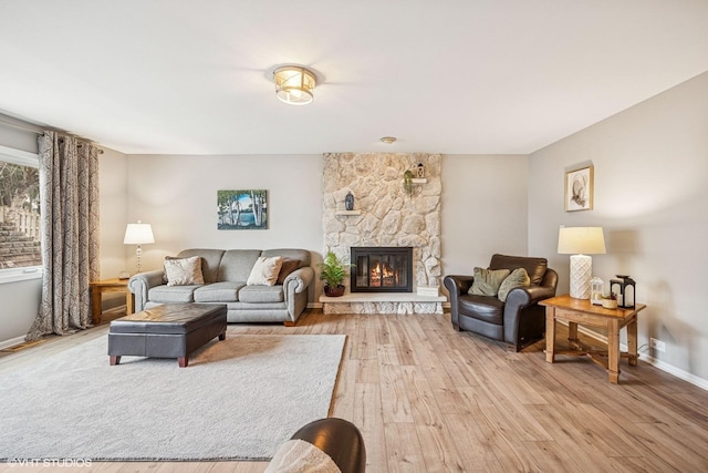 living room featuring light wood-style flooring, baseboards, and a stone fireplace